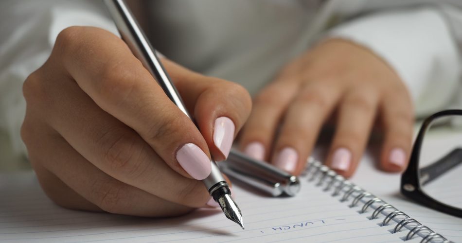 woman in white long sleeved shirt holding a pen writing on a paper